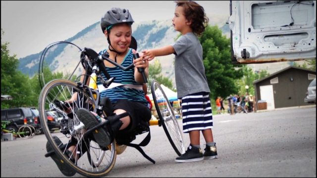 Photo of a toddler standing next to a woman on a recumbent bicycle