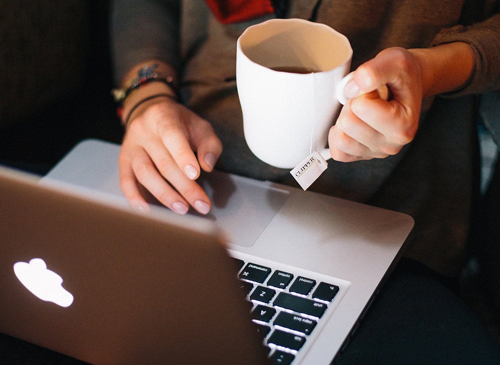 I mage of adult holding a mug of tea on working on a laptop