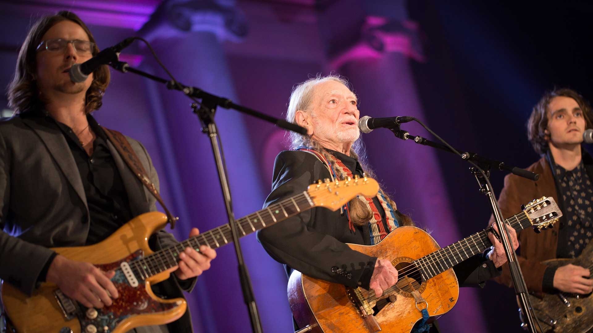 Willie Nelson singing on stage with a guitar