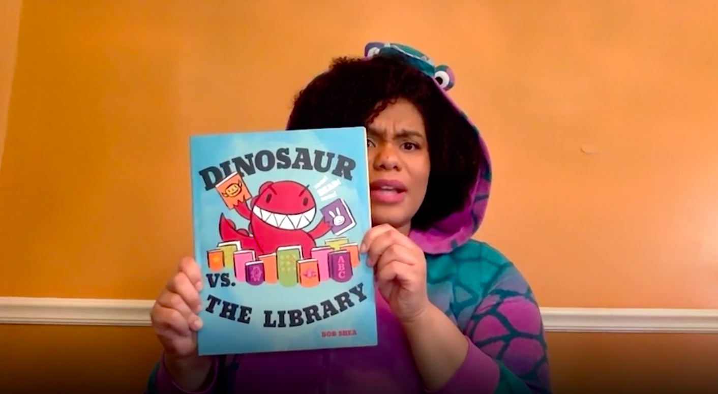 Woman in dinosaur costume reading childrens book