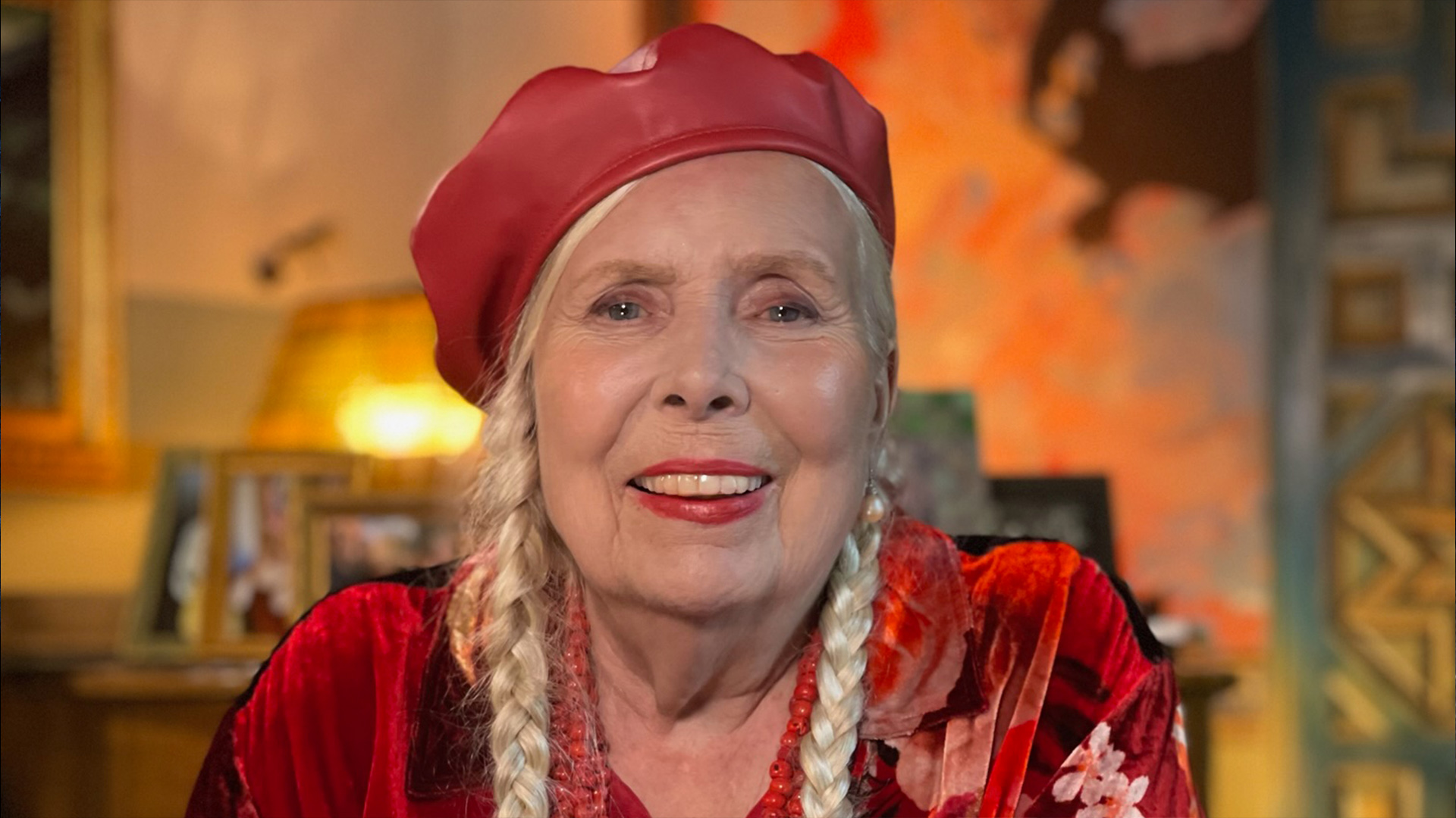 Joni Mitchell smiles in a red hat and blouse