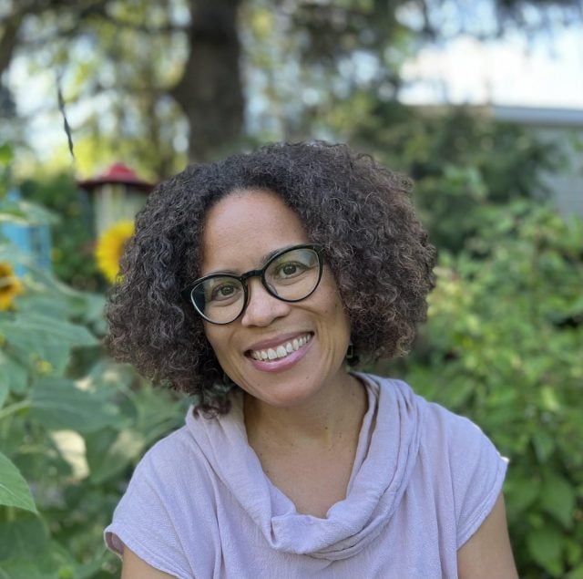 photograph of woman with glasses and curly hair smiling in garden